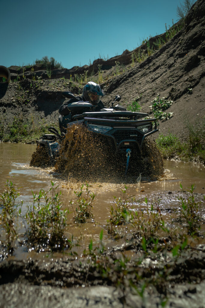 SPORTIVA 620 GT ATV durchquert schlammiges Wasser im Gelände – Offroad-Action mit Wasser-Splash und sportlichem Fahrer.
