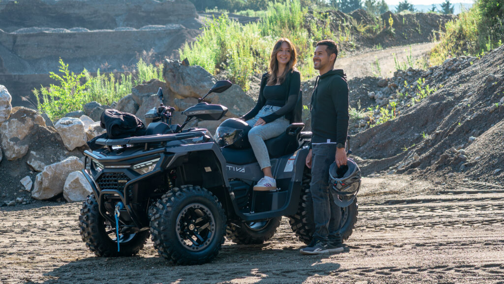 Mann und Frau mit SPORTIVA 620 GT ATV im Gelände, entspannter Moment vor der Fahrt bei sonnigem Wetter.