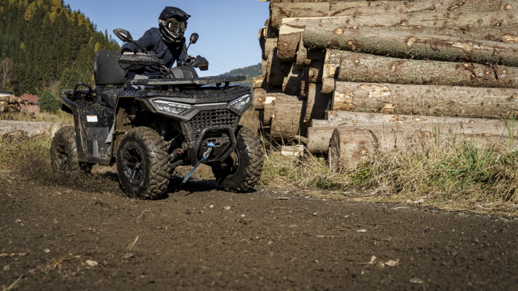 Schwarze SPORTIVA 520 GT im Offroad-Einsatz auf schlammigen Waldweg neben Holzstapel